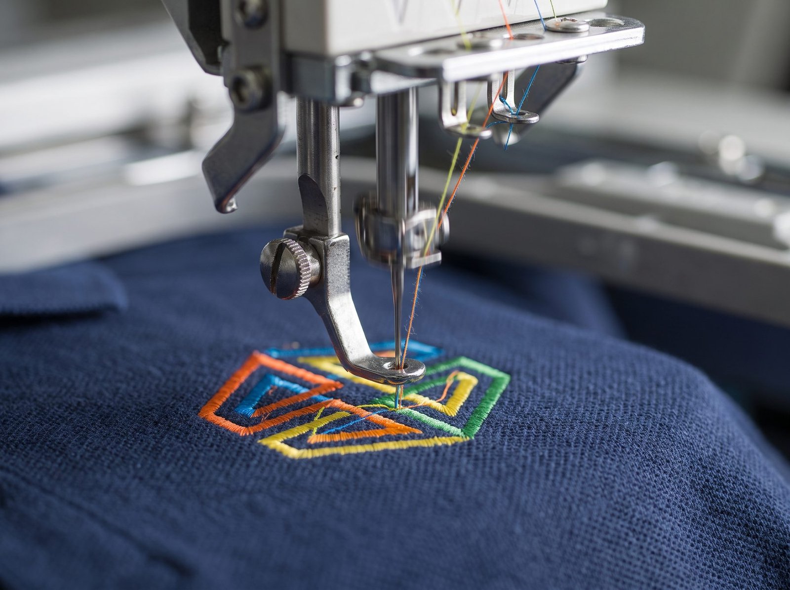 Macro close-up of an embroidery machine stitching a logo design onto navy polo fabric